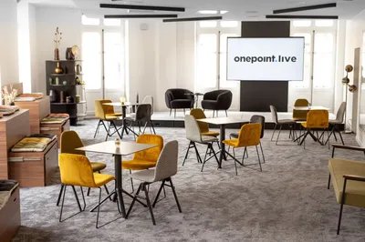 La salle de Onepoint Live : tables hautes, fauteuils jaunes et grand écran.